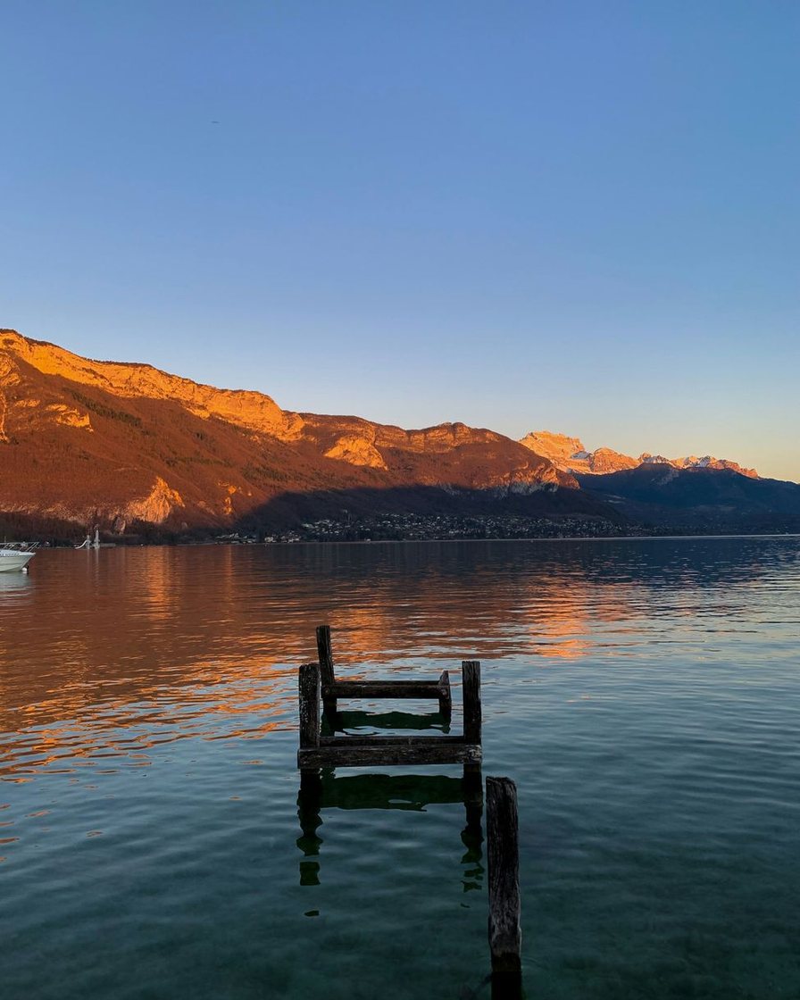 Table de restaurant en terrasse au bord du lac d'Annecy au coucher du soleil, verres de vin blanc, lac orangé et silhouette du château de Duingt au loin